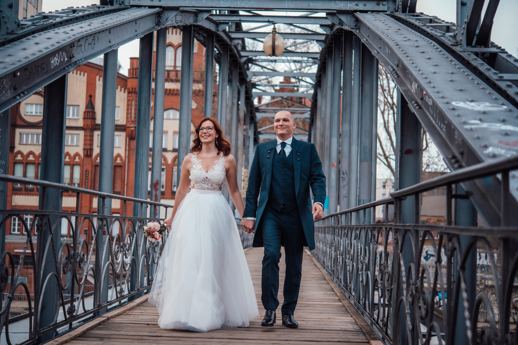 Hochzeitspaar Hand in Hand auf einer Stahlbrücke